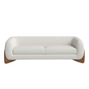 A front view of the Amala sofa, featuring a curved body in cream bouclé fabric that is cradled by a sculptural, solid wood base.