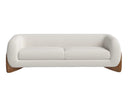 A front view of the Amala sofa, featuring a curved body in cream bouclé fabric that is cradled by a sculptural, solid wood base.