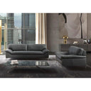 The Giorgia leather sofa and matching armchair in black, styled in a modern high-rise living room with a city skyline visible through large windows. The scene includes a glass coffee table, a textured grey rug, and large abstract art on the wall.