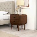 Wooden nightstand with two drawers next to a bed in a bedroom setting.