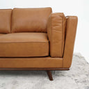 Tan leather sofa on a textured gray rug with a white background