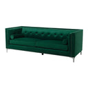 Three-quarters view of a luxurious emerald green velvet sofa, tufted and adorned with silver studs, includes matching bolster pillows on a white background.