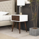 Hexagonal nightstand with wooden legs and white top next to a bed in a bedroom setting.