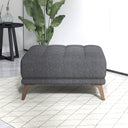 Dark gray upholstered ottoman with wooden legs in a room with a plant and small table.