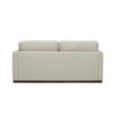 Rear view of a Bobbi upholstered loveseat in a light beige or cream-colored fabric, with two loose back cushions, a single bench seat cushion, slim arms, and a dark, continuous wooden base.
