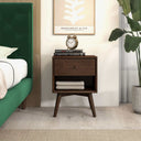 Wooden nightstand with books and a clock next to a green bed in a room with a plant.