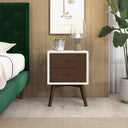 Wooden nightstand with two drawers next to a green upholstered bed in a bedroom setting.