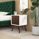 White nightstand with wooden drawers next to a green upholstered bed in a bedroom setting.