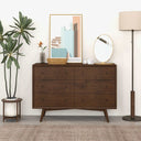 Wooden dresser in a room with a plant, lamp, and decorative items.