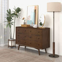 Wooden dresser with decorative items in a room setting with a plant and lamp.