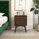 Wooden nightstand with lamp and mug next to a green upholstered bed in a bedroom.