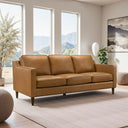 Tan leather sofa in a modern living room with large windows and decorative elements.