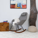 Gray rocking chair in a room with wooden side table, pouf, and abstract painting.