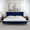 Modern bedroom with a blue upholstered bed, white bedding, and mountain-themed artwork.