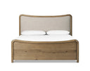 A heritage-inspired bed with soft curves and intricate carving along a rustic oak frame, featuring a light, linen-upholstered headboard.