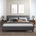 Dark gray upholstered bed in a bedroom with two lamps and framed art on the wall.