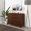 Wooden dresser in a room with a plant, lamp, and framed pictures.