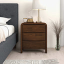 Wooden nightstand with decorative items next to a bed in a bedroom setting