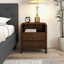 Wooden nightstand with books and a clock next to a bed in a bedroom setting.