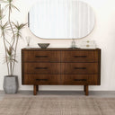 Wooden dresser with four drawers, a large round mirror above, and decorative items on a neutral background.