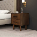 Wooden nightstand with two drawers next to a bed in a bedroom setting.