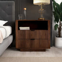Wooden nightstand with books and a lamp next to a bed in a bedroom setting.