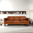Cognac leather sofa in a modern living room setting with a shelf and lamp.