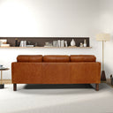 Rear view of a cognac leather sofa in a modern living room with a shelf and lamp in the background.