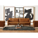 Brown sofa in a living room with abstract art and a shelf.