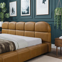 Tan leather bed in a room with green walls, framed pictures, and plants.