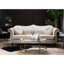 Front view of a Skein traditional three-seater sofa in light cream velvet, featuring a button-tufted camelback, two round throw pillows, rolled arms with nailhead trim, and dark turned legs in a living room set.