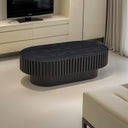 Black textured oval coffee table in a modern living room setting with a television and curtains.