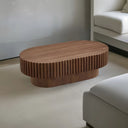 Front view of a walnut oval wooden coffee table with ribbed surface in a minimalistic living room.