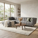 Adele 103-inch ash grey fabric left-facing sectional sofa with channel tufting and tapered wooden legs, styled with sage green pillows, a cream knit throw blanket, and a round wooden coffee table on an off-white shag rug in a modern living room.