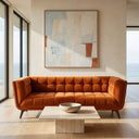 Modern living room featuring the Adele 85-inch burnt orange velvet sofa, styled with a travertine coffee table, large abstract wall art, and floor-to-ceiling windows with an ocean view.