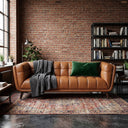 Adele 85-inch cognac top-grain leather sofa with channel tufting, styled with a grey cable-knit throw blanket and green velvet pillow in an industrial loft with an exposed brick wall and vintage area rug.