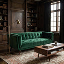 Adele emerald green velvet tufted sofa in a luxury study with dark wood paneled walls and built-in bookshelves, featuring a brass floor lamp and a wooden coffee table on a patterned rug.