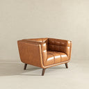 Mid-century modern accent armchair upholstered in rich cognac brown leather with grid-tufted stitching along the seat cushion and curved backrest, supported by tapered dark wood legs against a neutral beige background.