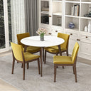 Modern round white dining table with dark wood legs, surrounded by four mustard yellow upholstered chairs and a vase of pink tulips on a textured rug in a bright dining area.
