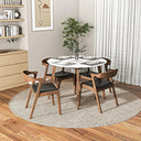 Round dining table with a white tabletop and wooden legs, surrounded by four mid-century wooden dining chairs with black cushioned seats on a round woven rug.
