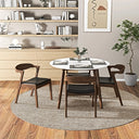 Modern round dining table with a white top and wood legs, surrounded by four wooden chairs with black cushioned seats, set on a round woven rug in a stylish dining room.
