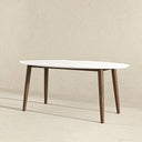 Adnan 67-inch mid-century modern oval dining table with a smooth white tabletop and tapered dark wood legs against a neutral background.
