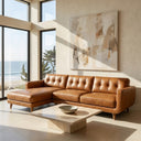 Adriana 111-inch tan genuine leather left-facing sectional sofa with button-tufted back cushions and tapered wooden legs in a sunlit modern living room overlooking the ocean.