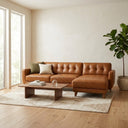 Adriana 111-inch tan genuine leather right-facing sectional sofa with tufted back cushions in a modern living room styled with a wooden coffee table, accent pillows, geometric patterned rug, and potted plant.