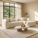 Agnes 113-inch ivory tufted chenille modular sectional sofa with chaise and accent pillows styled in a sunlit neutral living room with an organic stone coffee table and large windows.