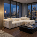 Agnes 113-inch ivory tufted chenille modular sofa with matching ottoman styled in a modern high-rise living room featuring floor-to-ceiling city skyline views at night, a black marble coffee table, and a brass floor lamp.