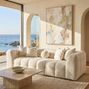 Agnes 90-inch tufted ivory chenille sofa in a modern coastal living room with ocean views, featuring a travertine coffee table and abstract wall art.