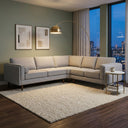 Allegra 105 light grey fabric corner sofa styled in a modern living room on a cream textured rug, illuminated by an arched brass floor lamp with city views at night.