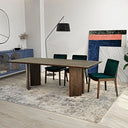 Almaza 87-inch walnut dining table with slab pedestal legs, paired with dark green velvet upholstered chairs on a patterned rug in a modern room setting.
