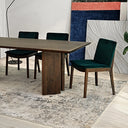 Almaza 87-inch walnut dining table with solid slab legs, surrounded by dark green velvet upholstered chairs on a textured neutral rug in a modern dining space.

